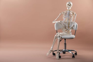 Açık kahverengi arkaplan üzerinde oturan yapay insan iskelet modeli, metin için boşluk