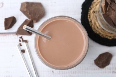 Tasty chocolate milk in glass and pieces of chocolate on white wooden table, flat lay