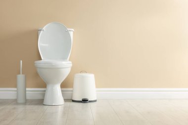 Tuvalet, fırça ve çöp tenekesi tuvalette bej duvarın yanında, mesaj için yer var.