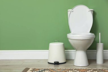 Yeşil duvarın yanında seramik klozet, fırça ve çöp tenekesi. Metin için boşluk