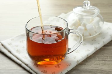 Tahta masada çaydanlıktan fincana taze demlenmiş çay dökülüyor, yakın plan.