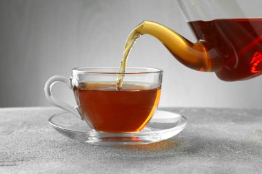 Gri masada çaydanlıktan fincana taze demlenmiş çay dökülüyor, yakın plan.