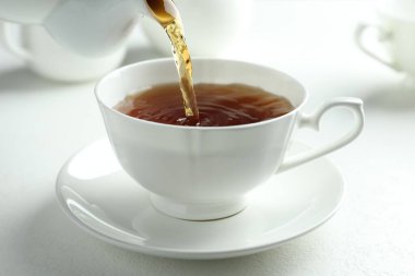 Beyaz masada çaydanlıktan fincana taze demlenmiş çay dökülüyor, yakın plan.