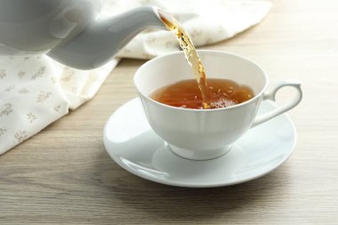 Ahşap masada çaydanlıktan fincana aromatik çay dökülüyor.