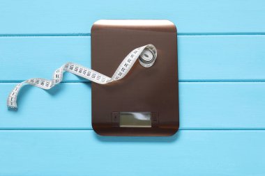 Elektronik mutfak ölçeği ve mezura açık mavi ahşap masa, üst manzara. Diyet