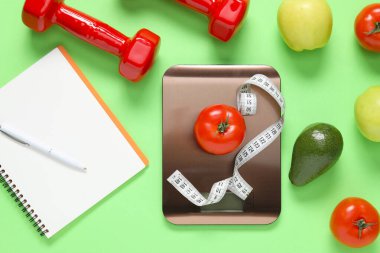 Elektronik mutfak ölçeği, mezura, dambıl, not defteri ve açık yeşil arka plandaki ürünler, düz yatak. Kalori kontrolü