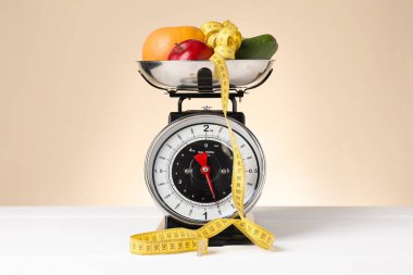 Bej arka planda beyaz ahşap masa üzerinde bir kase mezura ve ürünlerle mekanik mutfak tartısı