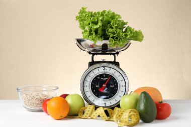 Ürünlerle birlikte mekanik mutfak terazisi ve bej arka planda beyaz ahşap masadaki şerit. Diyet