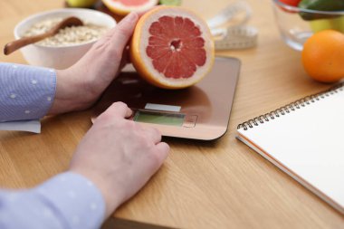 Mutfak terazisinde greyfurt tartan bir kadın ahşap masada, yakın plan.