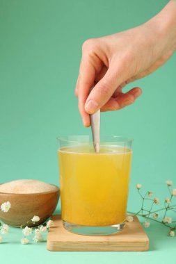 Turkuaz arka planda suda kolajen tozu karıştıran kadın, yakın plan.