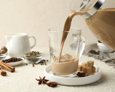 Beyaz desenli masada cam fincana aromatik Masala çayı dökülüyor, yakın plan.