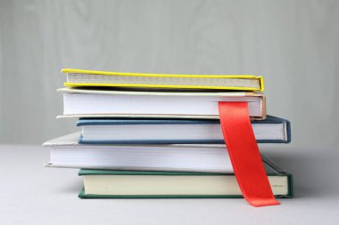 Açık gri masadaki renkli olanlar arasında kırmızı kurdele yer imi olan kitap, yakın plan