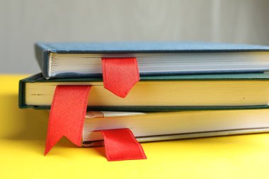 Sarı masadaki kırmızı kurdele yer imlerine sahip kitaplar gri arkaplanda, yakın plan