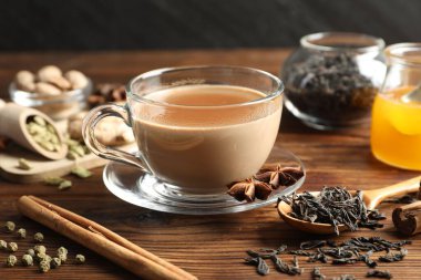 Aromatik Masala çayı fincanda, baharatlar, kuru yapraklar ve bal ahşap masada, yakın plan.