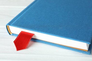 Beyaz ahşap masa üzerinde kırmızı kurdele yer imi olan kitap, yakın plan.