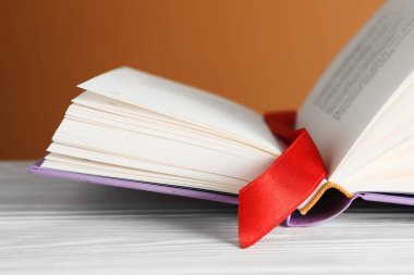 Kahverengi arkaplana karşı beyaz ahşap masa üzerinde kırmızı kurdele yer imi olan kitabı aç, kapat