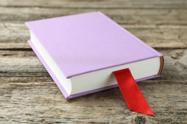 Ahşap masada kırmızı kurdele yer imi olan bir kitap, yakın plan.