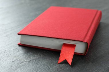 Koyu desenli masa üzerinde kırmızı kurdele yer imi olan kitap, yakın plan.