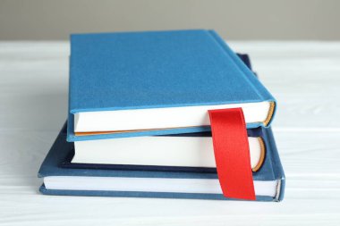 Kırmızı kurdele yer imi ve beyaz ahşap masa üzerinde renkli kitap gri arkaplan, yakın plan