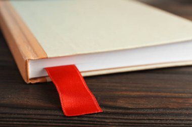 Ahşap masada kırmızı kurdele yer imi olan bir kitap, yakın plan.