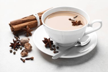Aromatik Masala çayı fincanda ve baharatlar açık gri masada, yakın plan.