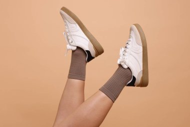 Bej arka planda şık kahverengi çoraplı ve spor ayakkabılı kadın, yakın plan.