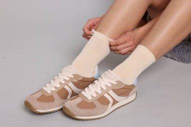 Açık gri arka planda şık bej çoraplı ve spor ayakkabılı kadın, yakın plan.