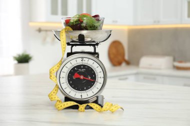 Salatalı mutfak terazileri ve kapalı alandaki hafif mermer masada mezura.