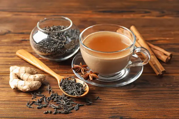 Bardakta Aromatik Masala çayı, ahşap masada baharatlar ve kuru yapraklar, yakın plan.