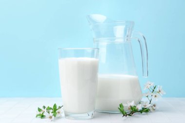 Taze süt ve çiçekler beyaz masada açık mavi arka planda