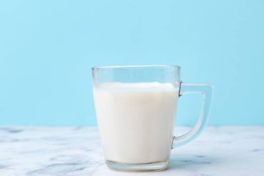 Açık mavi arka planda beyaz mermer masada bir fincan süt.