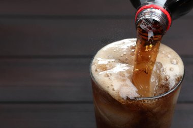 Ahşap masada şişeden bardağa ferahlatıcı kola doldurmak, yakın plan. Metin için boşluk