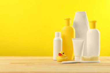 Bebek kozmetik ürünleri ve banyo aksesuarları ahşap masada, sarı arka planda. Metin için boşluk