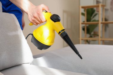 Temizlikçi kanepeyi evde buharlı temizleme makinesiyle temizliyor.