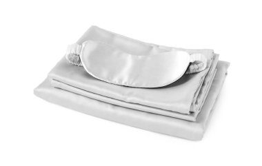 Beyaz arka planda ipeksi çarşaf ve uyku maskesi yığını