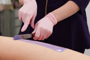 Profesyonel kozmetik uzmanı, kuaförde saç çıkarma prosedüründen önce müşterinin bacağına sıcak tüy dökücü krem sürüyor.