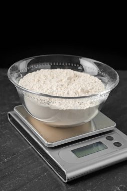 Elektronik mutfak terazisi ve koyu renkli bir kase un, siyah arka planda, yakın plan.