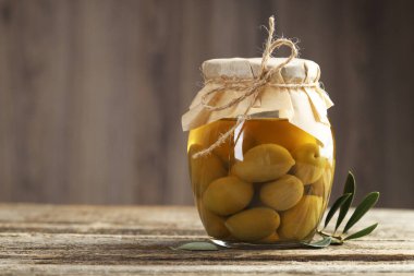 Cam kavanozda yeşil zeytin turşusu ve ahşap masada yapraklar. Metin için boşluk