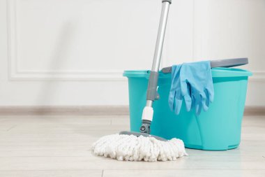 Beyaz duvarın yanındaki tahta zemine ip, kova ve eldiven. Metin için boşluk