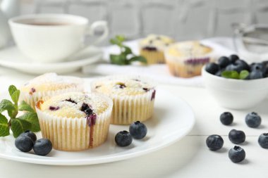 Yaban mersinli lezzetli kekler, pudra şekeri ve beyaz ahşap masada nane şekeri, yakın plan.