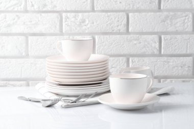 Different clean dishware on white table near brick wall