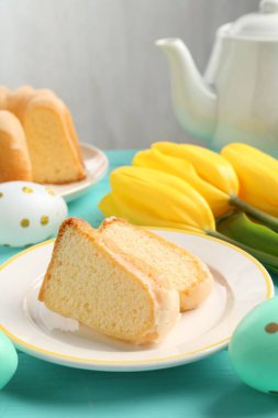 Lezzetli kek parçaları, paskalya yumurtaları ve laleler açık mavi ahşap masada, yakın plan.