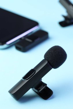 Açık mavi arkaplanda kablosuz alıcısı olan Lavalier mikrofon ve akıllı telefon, seçici odak