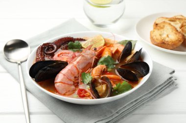 Beyaz ahşap masada servis edilen lezzetli deniz ürünleri çorbası, yakın plan.