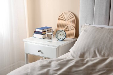Yatağın yanında kitap, dekor, bir bardak su ve çalar saat olan komodin.