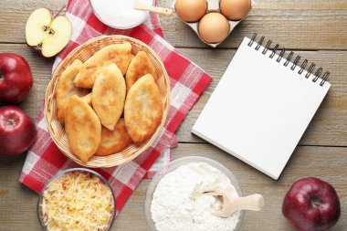 Boş tarif kitabı, kızarmış pirinçli börek (dolma turta) ve ahşap masa üzerindeki malzemeler.