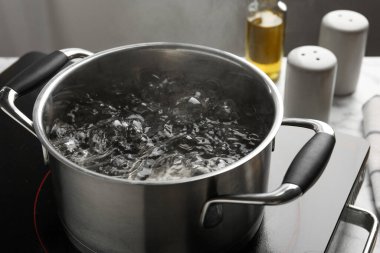 Kaynar suyla pişirme tenceresi ve beyaz masa üzerinde gri arka plan, yakın çekim