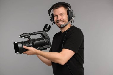 Profesyonel kameralı ve kulaklıklı bir adam gri arka planda.