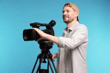 Açık mavi arka planda profesyonel video kamerası olan adam.