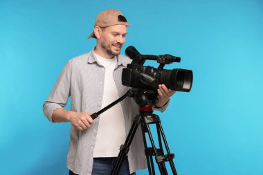 Açık mavi arka planda profesyonel video kamerası olan adam.